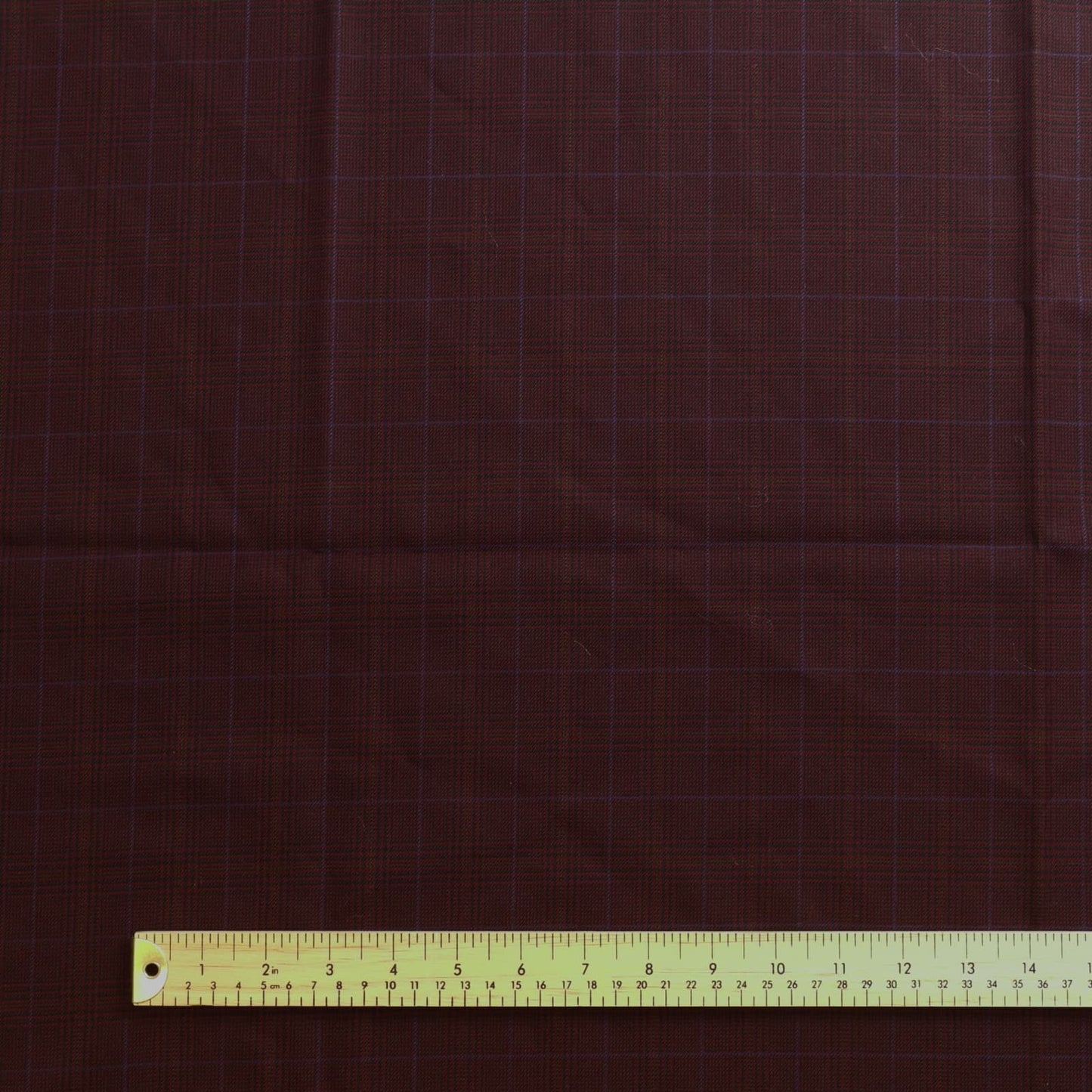 Dark red viscose polyester tartan suiting fabric laid flat with ruler for scale