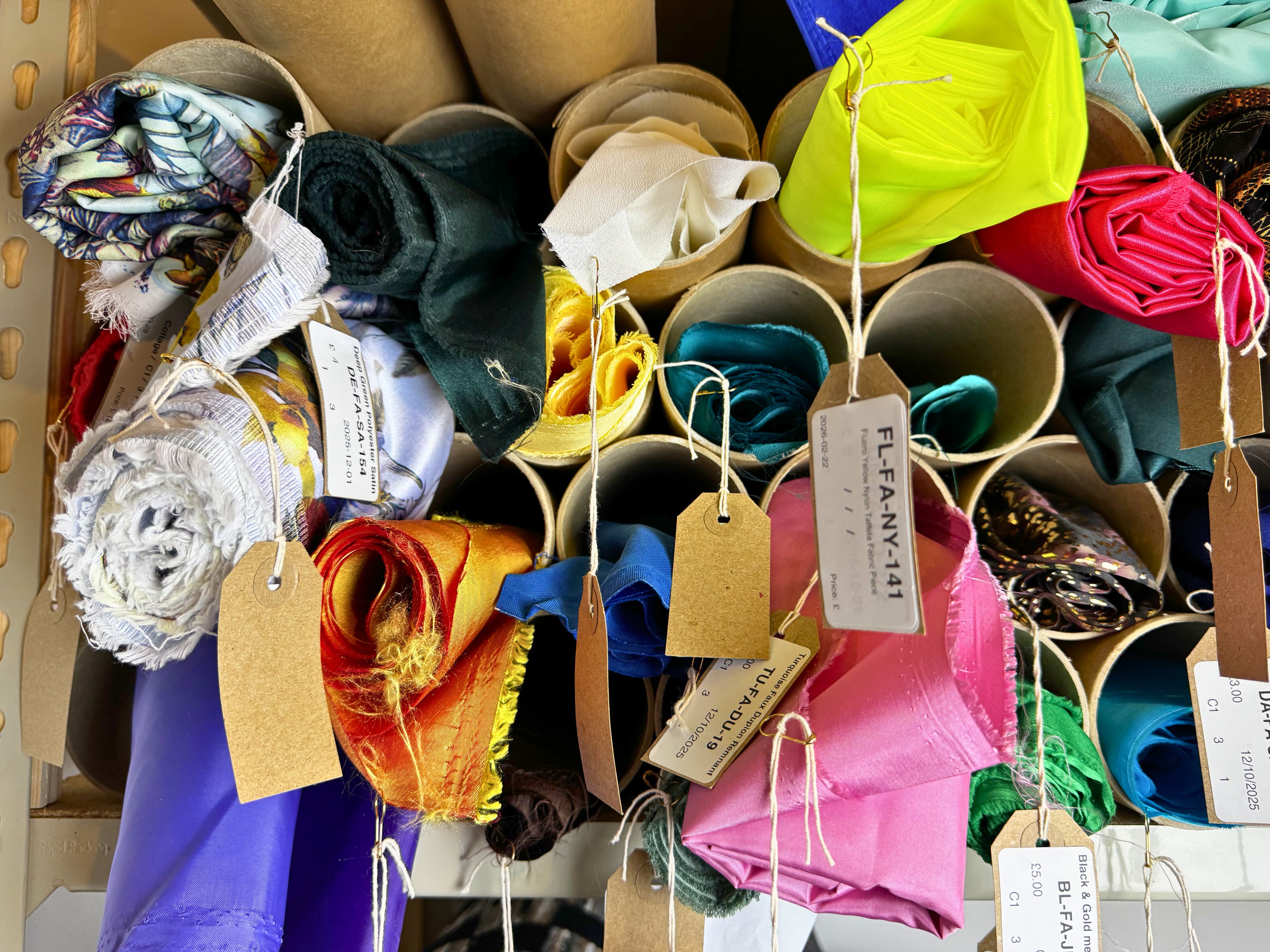 Colorful pre-loved dressmaking fabric in rolls with tags on a wooden surface